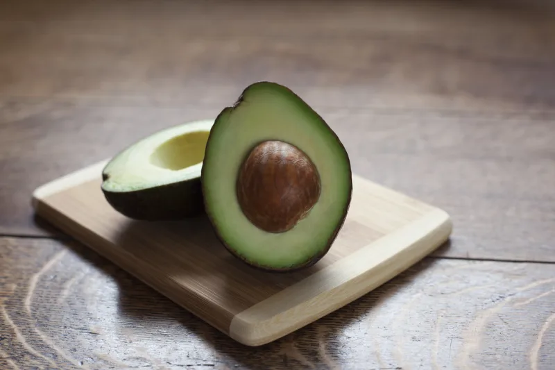 Avocado tăiat în jumătate pe un tocător de lemn, cu miezul verde și sâmburele vizibil