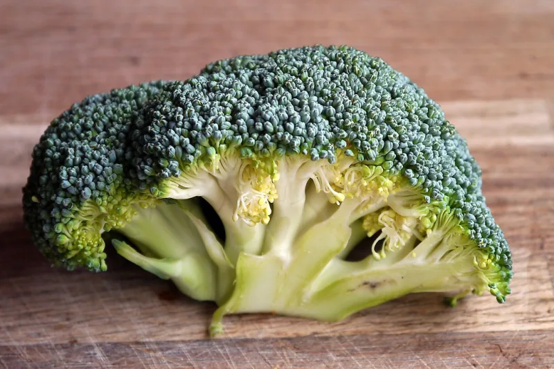 Căpățână de broccoli proaspăt, tăiată în jumătate, pe o masă din lemn