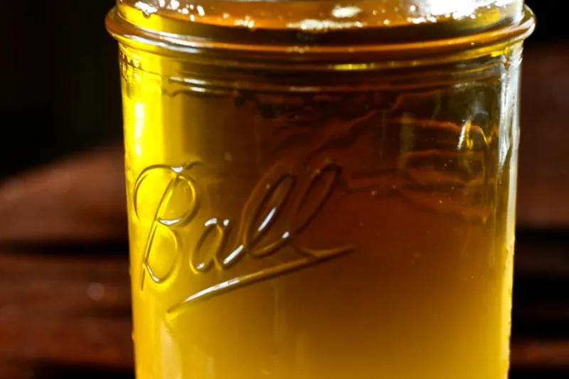 A glass jar filled with golden ghee, clarified butter, on a wooden table
