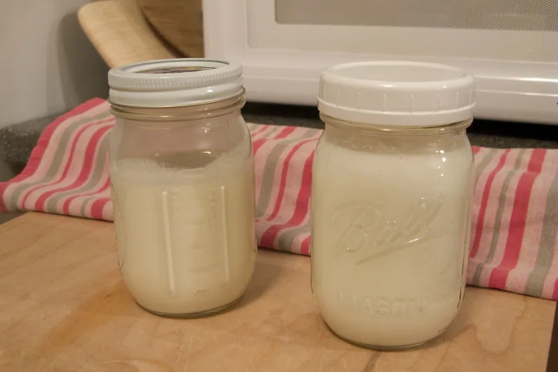Două borcane cu kefir de lapte proaspăt fermentat pe o masă de lemn