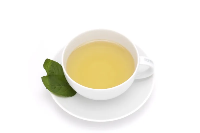 A cup of delicate white tea with a fresh green leaf beside it