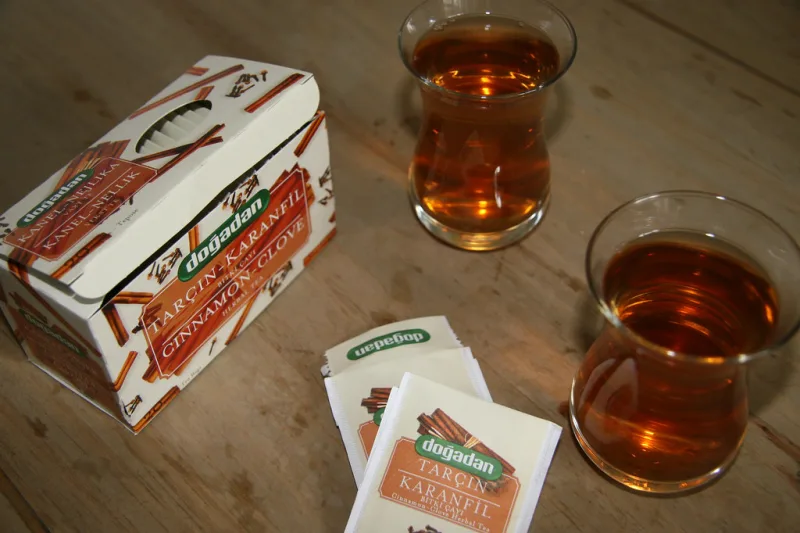Steaming clove tea in glasses next to a box of teabags and whole cloves