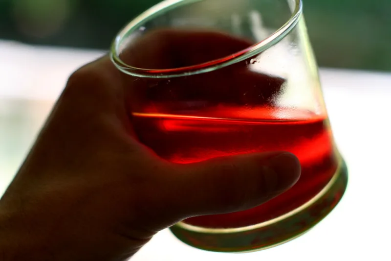 Glass of clear red hibiscus tea held in hand in natural light