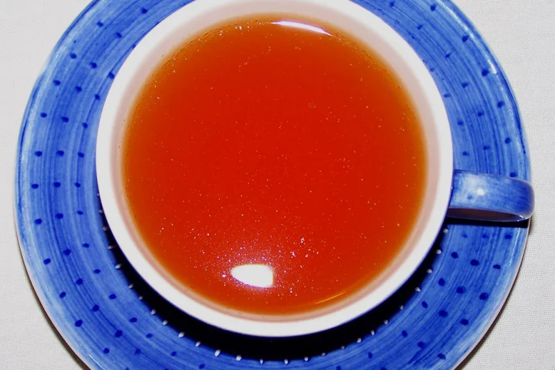 Ceașcă de ceai de rooibos roșu-chihlimbariu pe o farfurioară albastră