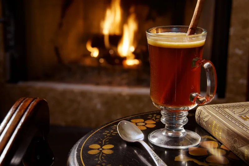 Cană de ceai de scorțișoară cald, cu băț de scorțișoară, lângă foc