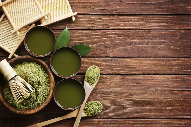 Pudră de matcha, ceai matcha preparat și tel de bambus pe o masă de lemn