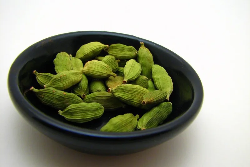 Green cardamom pods in a black ceramic bowl