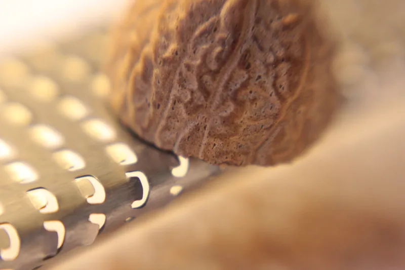A whole nutmeg seed resting on a metal grater, ready to be grated