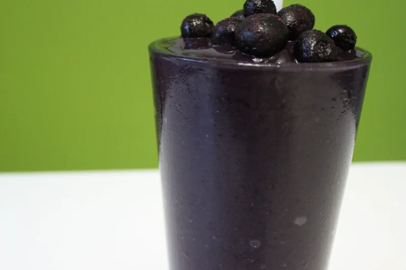Smoothie energizant cu afine proaspete într-un pahar pe fundal verde