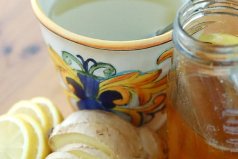 Cup of ginger tea with lemon slices, fresh ginger root and a jar of honey on a wooden table