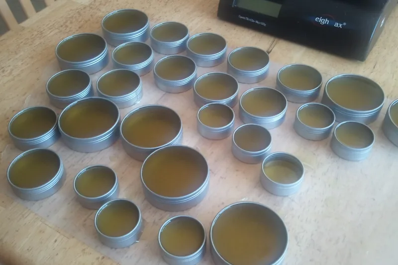Metal tins of homemade herbal salve on a wooden table