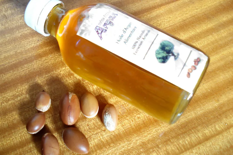 Sticluță cu ulei de argan auriu și fructe de argan pe masă de lemn